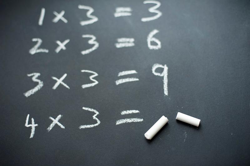 Beginning of the three times table written in chalk on a blackboard, with a broken piece of chalk against the last, unanswered sum